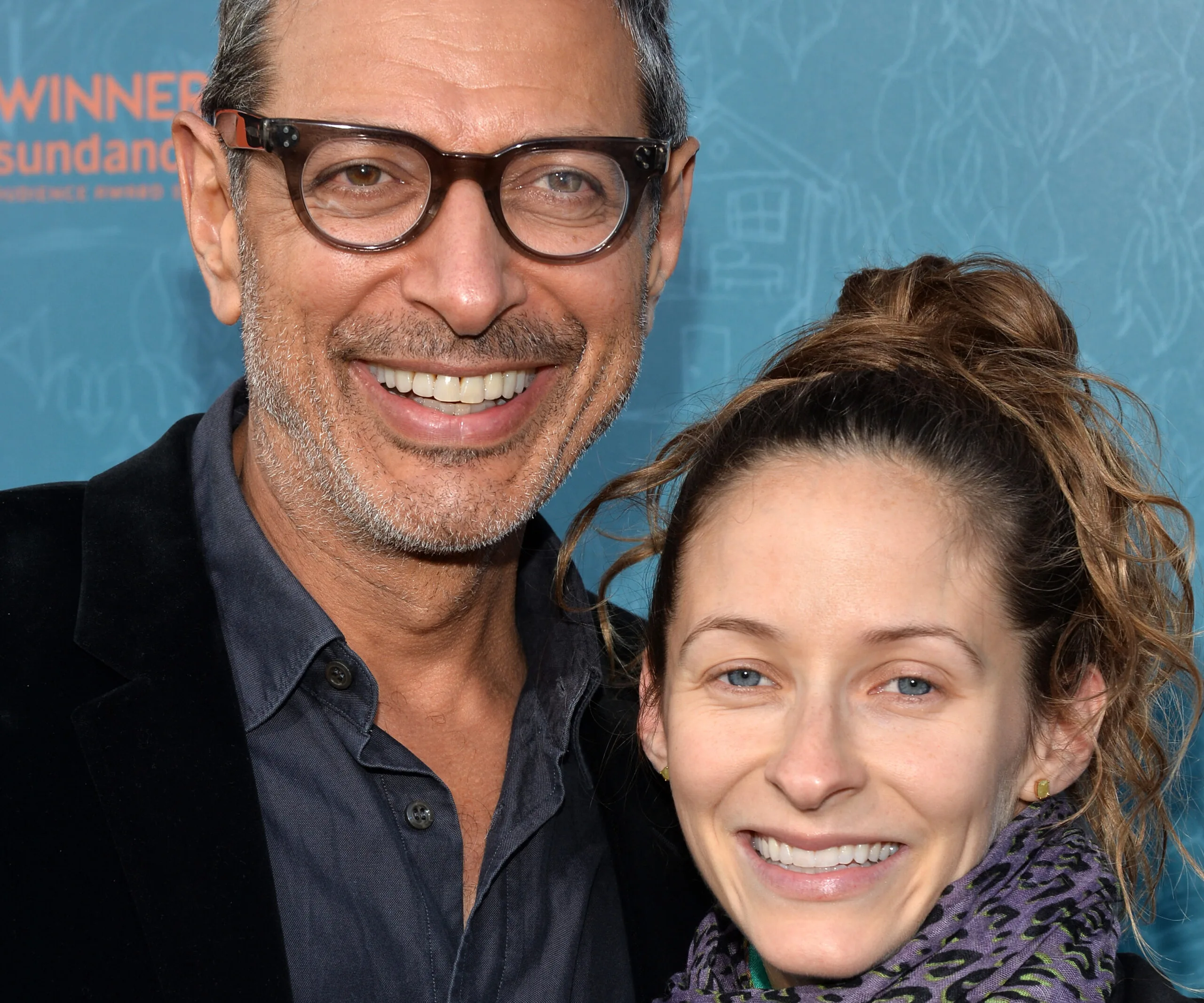 A smiling man in glasses and a woman with tied-back hair against a blue background.