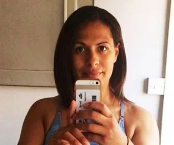 Woman taking a mirror selfie in a light blue tank top, holding a phone with a gold case.