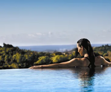 Woman relaxing in an infinity pool with a scenic view of the horizon and lush greenery in the background.