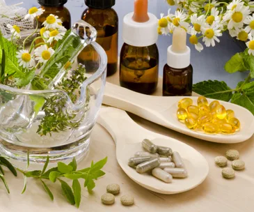 Herbal remedies with capsules, oil bottles, chamomile flowers, and fresh herbs in a mortar.