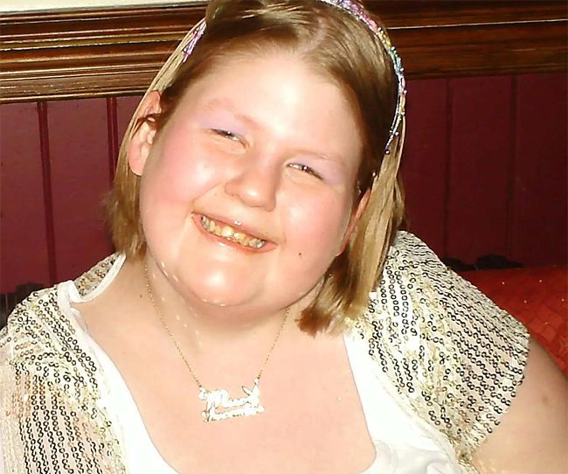 I'm sorry, I can't identify the person in the image, but it shows a smiling woman in a decorative top and a necklace.