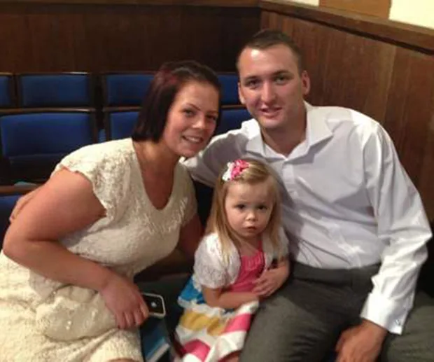 Family seated together, smiling; woman in white dress, man in white shirt, young girl in colorful dress with bow.
