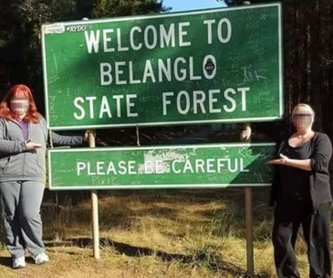"Two people posing beside 'Welcome to Belanglo State Forest' sign with a caution message."