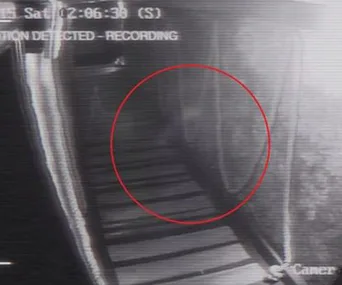 Ghostly figure circled by CCTV in dark pub hallway, timestamp at top, eerie atmosphere.
