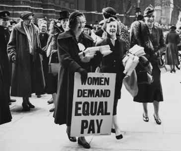 Women protest with a sign reading "Women Demand Equal Pay" in a historic demonstration for gender pay equality.
