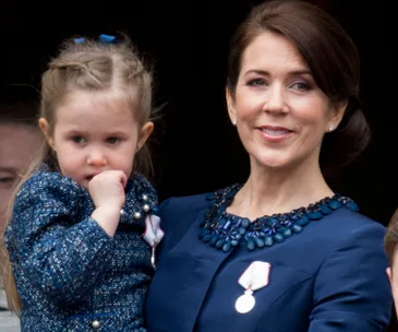 "Princess Mary holding her daughter with a thoughtful expression, both wearing blue outfits."