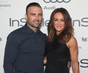 A man and woman smiling together on a red carpet at an event.