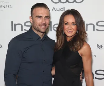 A man and woman smiling together on a red carpet at an event.