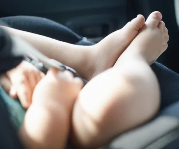 Baby feet in a car seat, blurred focus, sunny setting.