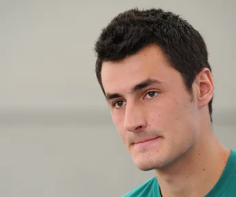 A person with short dark hair wearing a teal shirt, looking slightly to the side with a neutral expression.