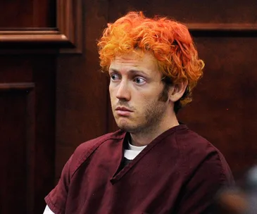 Courtroom scene with a person in a burgundy jumpsuit and dyed orange hair, appearing attentive.