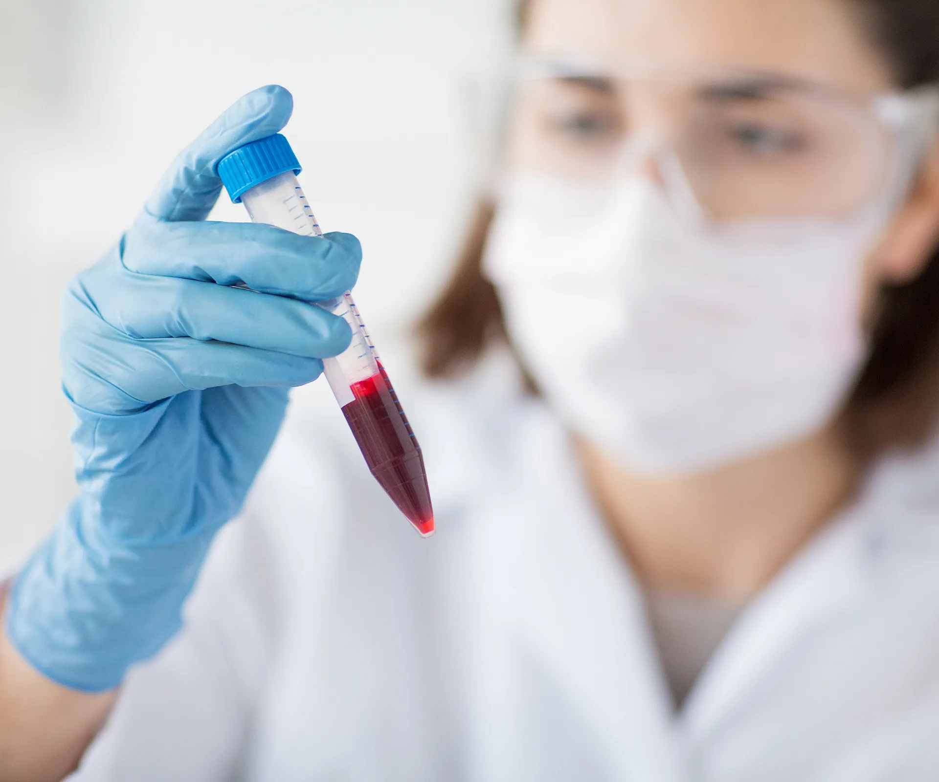 A scientist in protective gear examining a test tube with a red liquid.