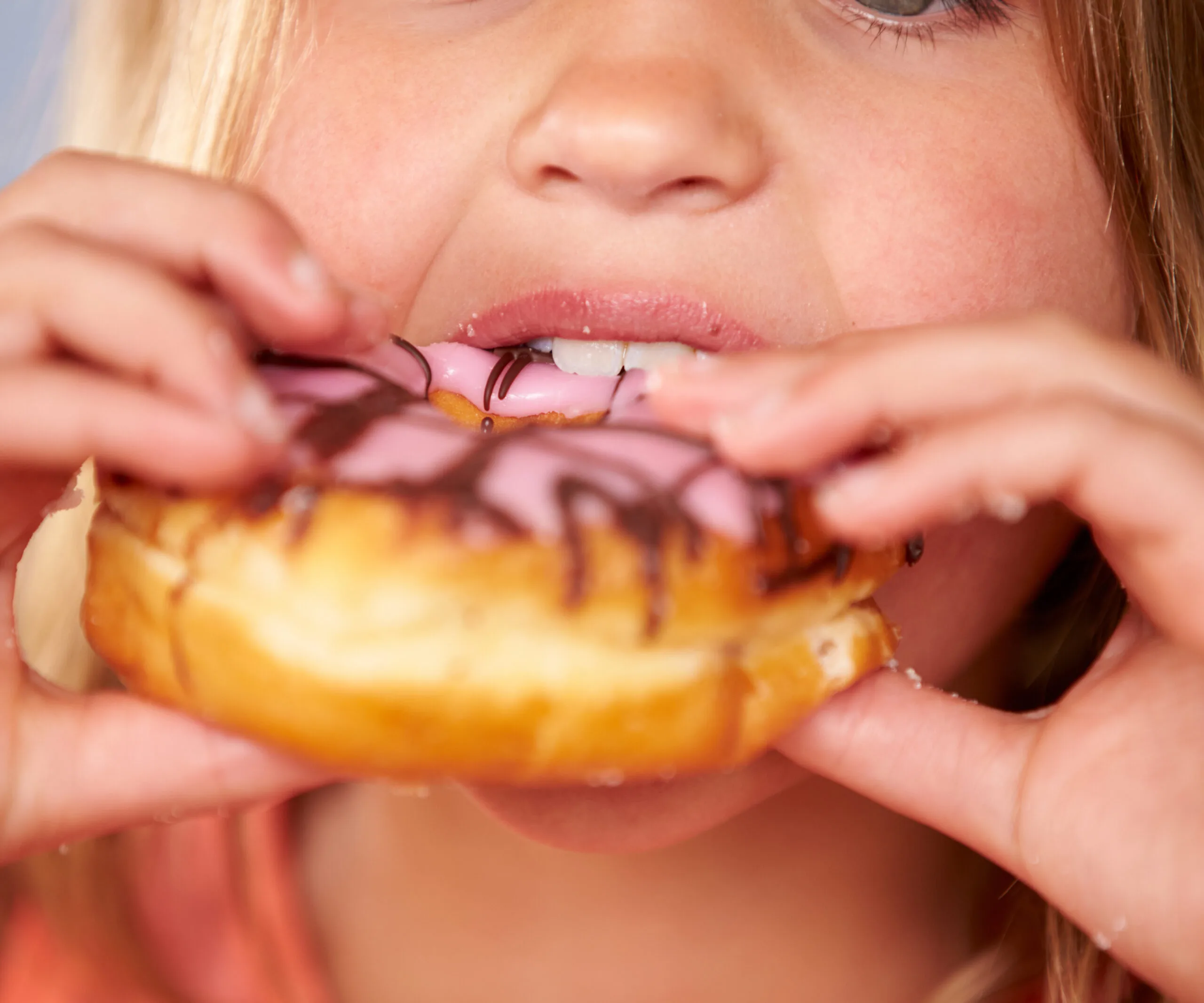 A child eating a donut with pink icing and chocolate drizzle close-up.