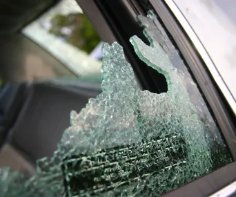 Shattered car window with jagged glass edges, indicating a break-in or emergency access.