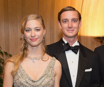 Two elegantly dressed individuals smiling; woman in a beaded dress, man in a tuxedo.