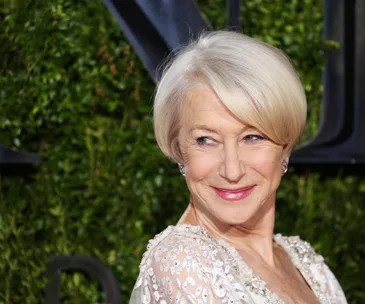 A woman with short blonde hair wearing an embellished dress, smiling slightly and looking to the side, with a green background.