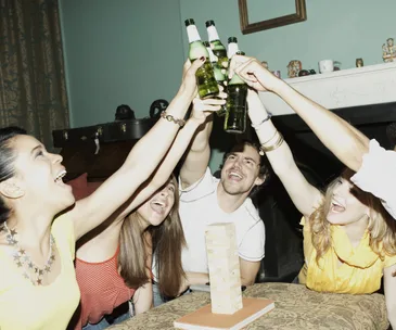 People raising beer bottles in a celebratory toast, gathered around a table with a Jenga tower.