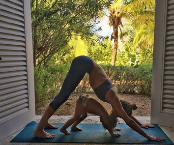 Woman and child doing yoga in downward-facing dog pose on a mat with a tropical backdrop.