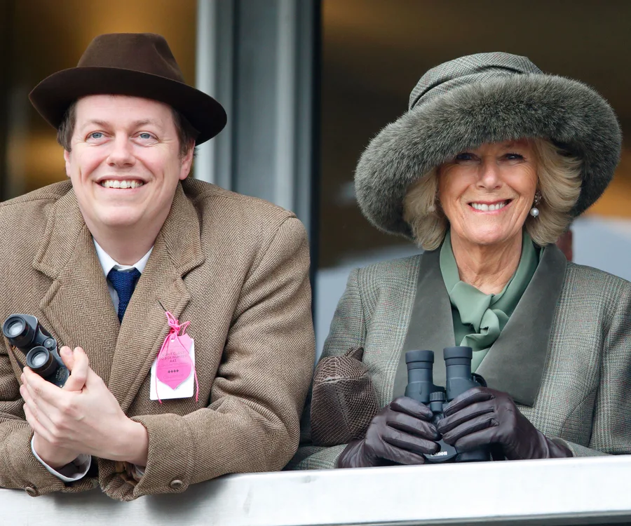 Two people in stylish coats and hats smiling at an outdoor event, both holding binoculars.