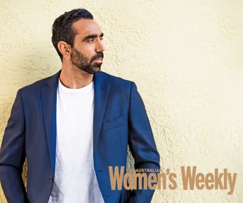 Alt text: "Man in blue blazer and white shirt standing against a yellow textured wall, looking to the right."