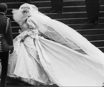 Bride in elaborate gown with long veil, ascending steps with entourage.