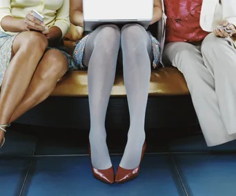 Three people sitting, only legs visible; center person using a laptop, with others holding phones.