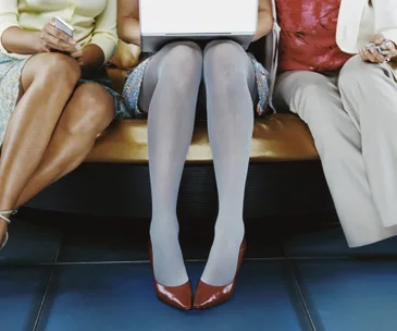 Three people sitting, only legs visible; center person using a laptop, with others holding phones.
