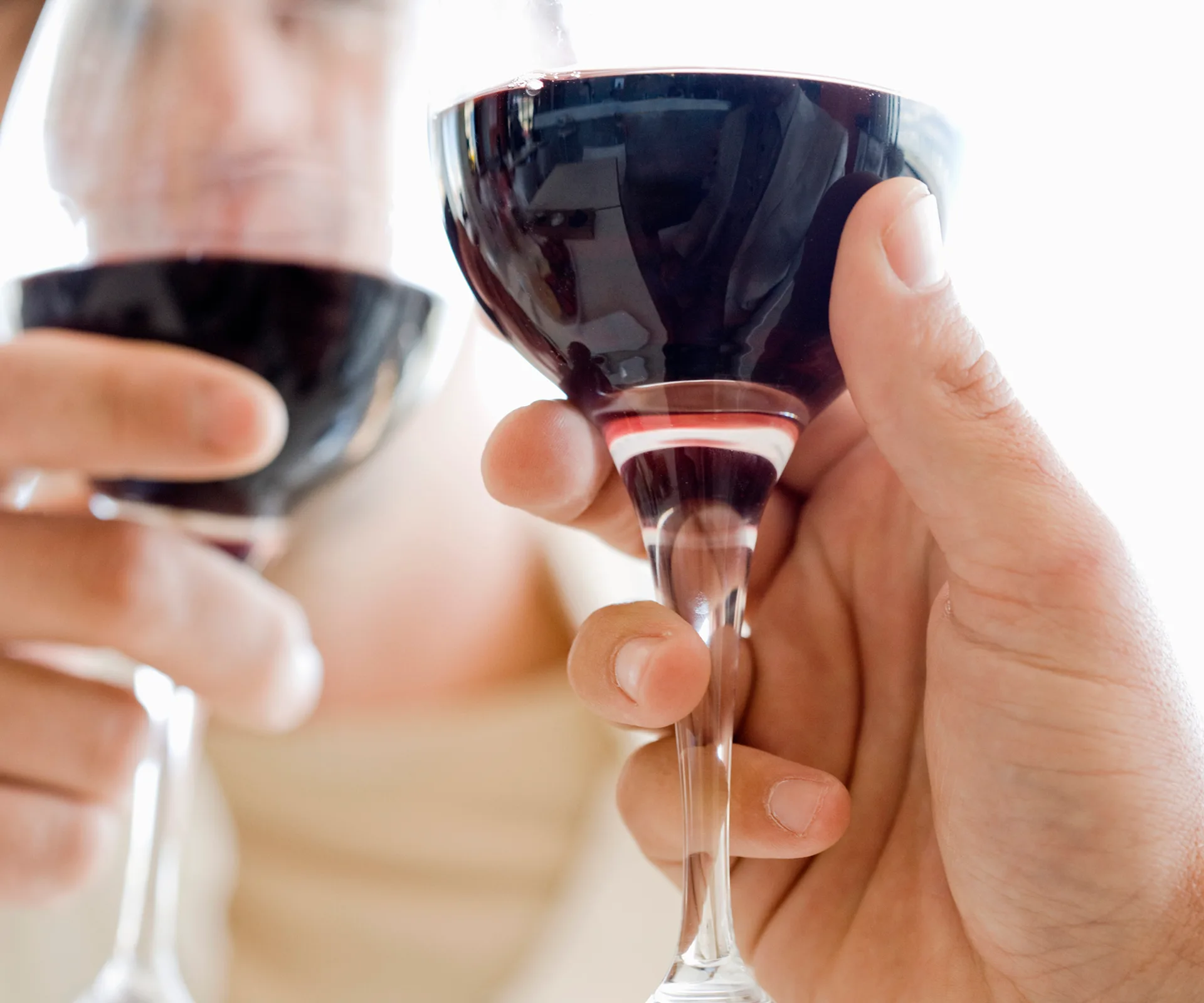 Two hands clinking wine glasses filled with red wine, close-up.
