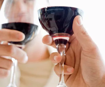 Two hands clinking wine glasses filled with red wine, close-up.