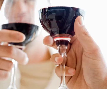 Two hands clinking wine glasses filled with red wine, close-up.