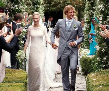 Bride and groom walk hand in hand down a garden aisle, surrounded by cheering guests and floral decorations.