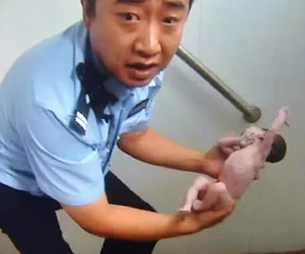 Police officer holds newborn baby rescued from a public toilet pipe.