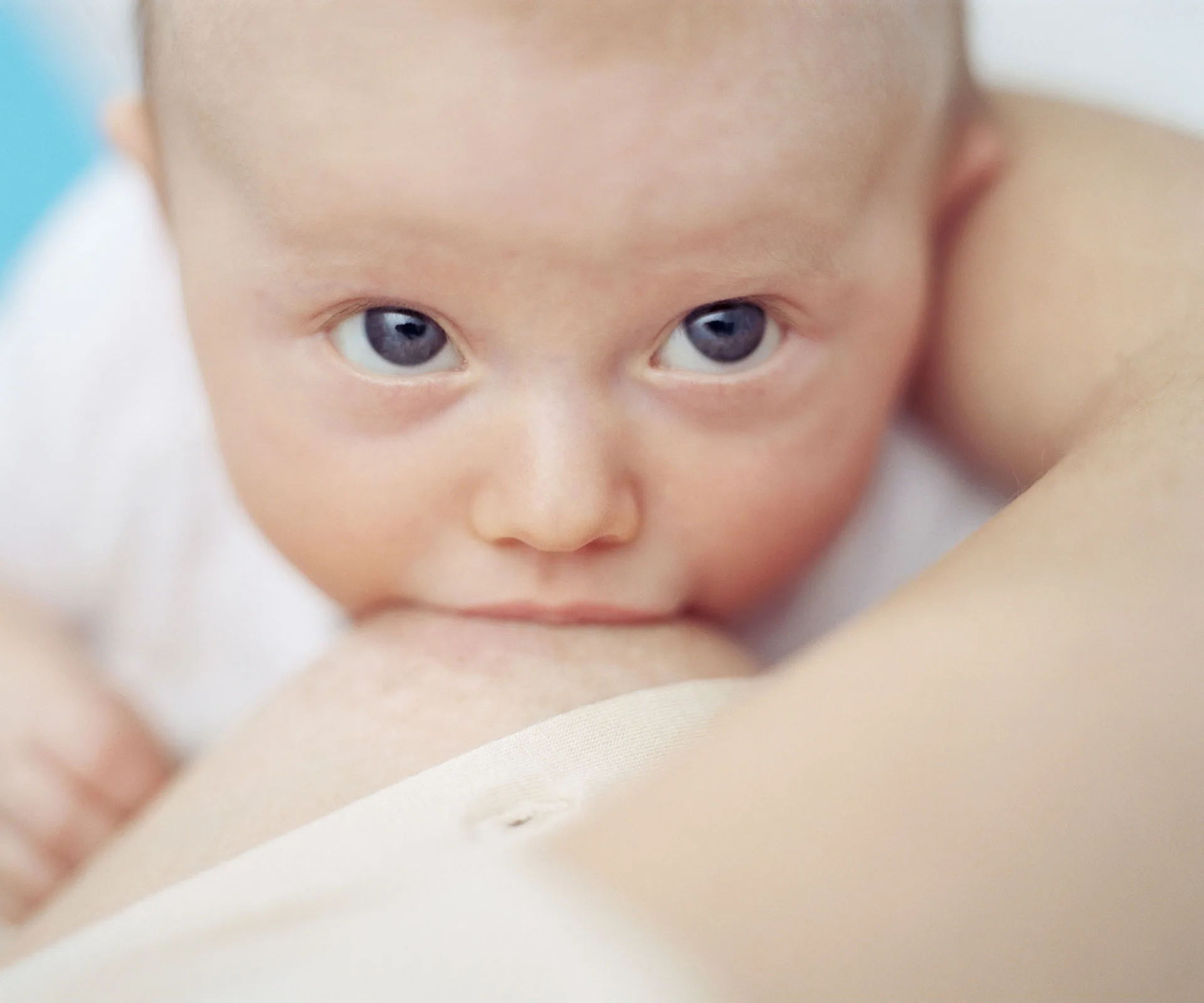 Baby breastfeeding, looking up towards the camera with wide eyes.