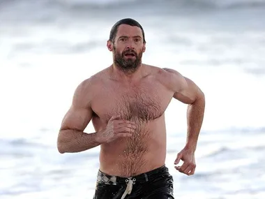 A man running shirtless on a beach with ocean waves in the background.