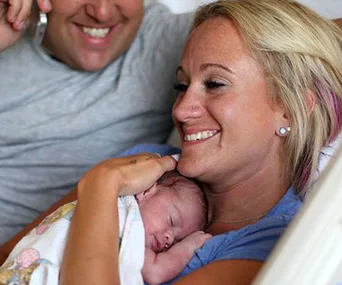 A couple joyfully embraces their adopted newborn for the first time, with the baby resting on the mother's chest.