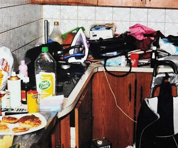Cluttered kitchen counter with various items, including plates, a plastic bottle, iron, and household products.