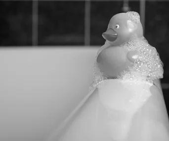 Rubber duck covered in bubbles, resting on the edge of a bathtub.