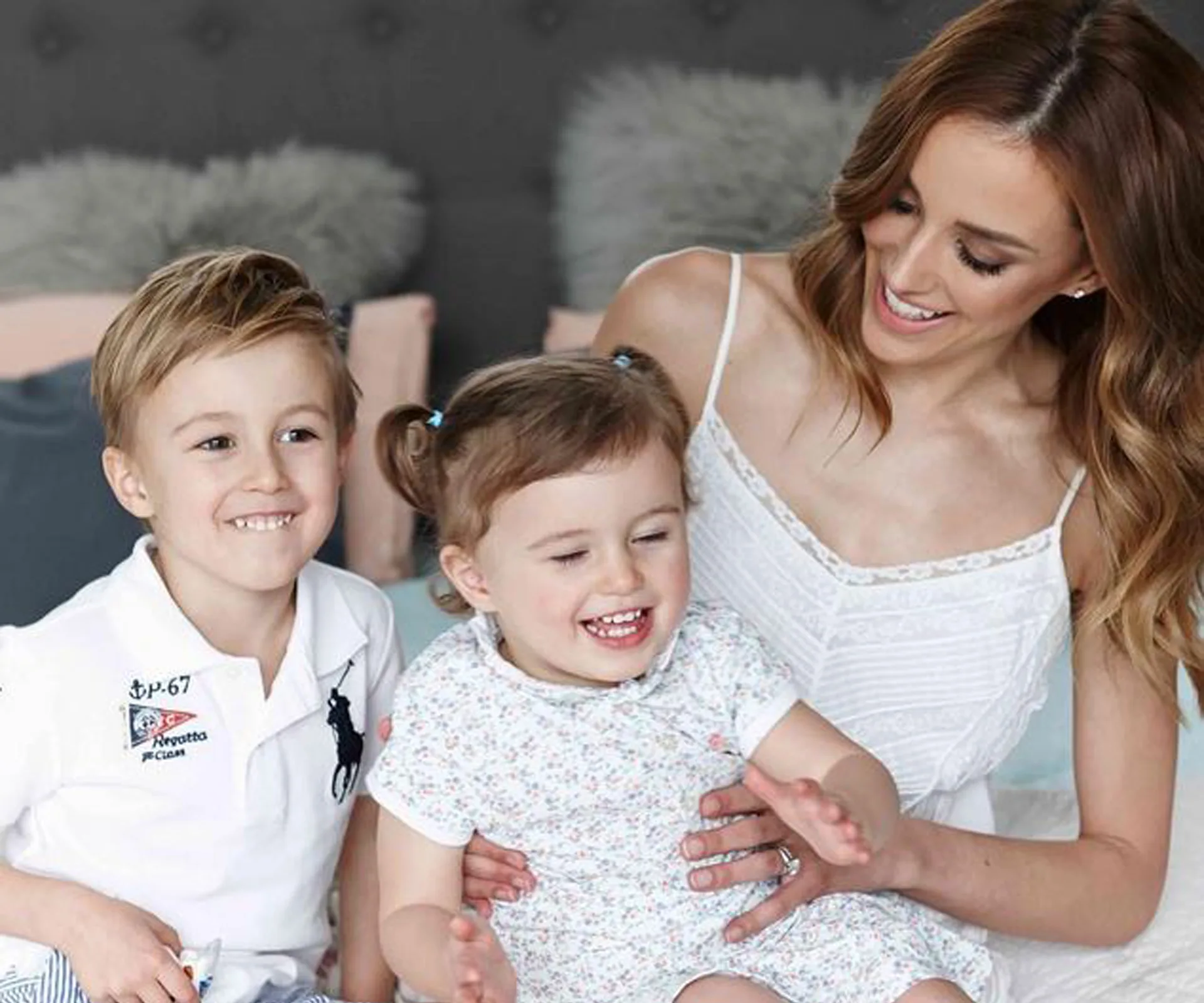 A woman smiling with two happy children seated on her lap.