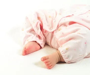A baby lying down in a pink onesie with small prints, showing their feet.