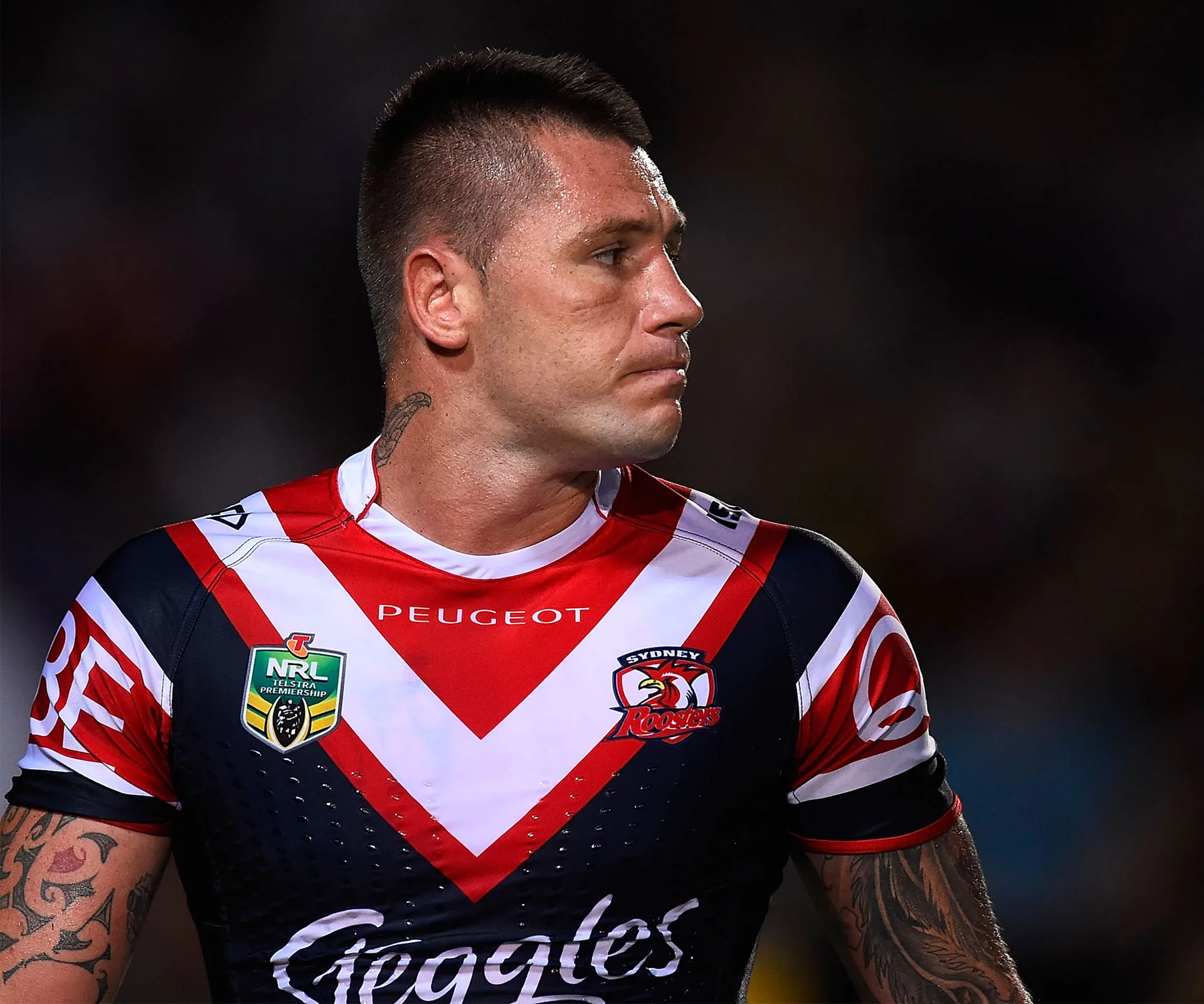 Rugby player in Sydney Roosters jersey with tattoos, looking to the side during a match.