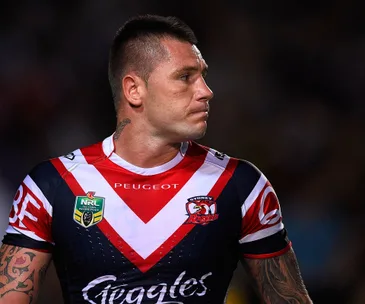 Rugby player in Sydney Roosters jersey with tattoos, looking to the side during a match.