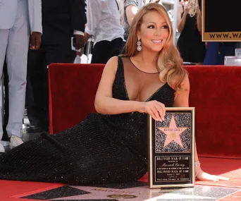 Mariah Carey poses with her Hollywood Walk of Fame star in a black dress on the red carpet.