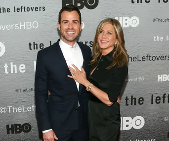 Man in a suit and woman in a black dress smiling at an event promoting "The Leftovers" on HBO.