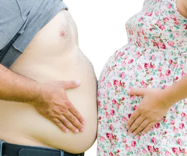 Man and woman touch their rounded stomachs; woman wears floral dress.
