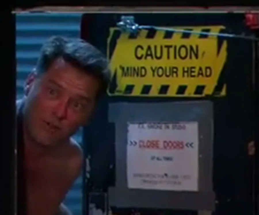 A man peeks over a door with caution signs visible.