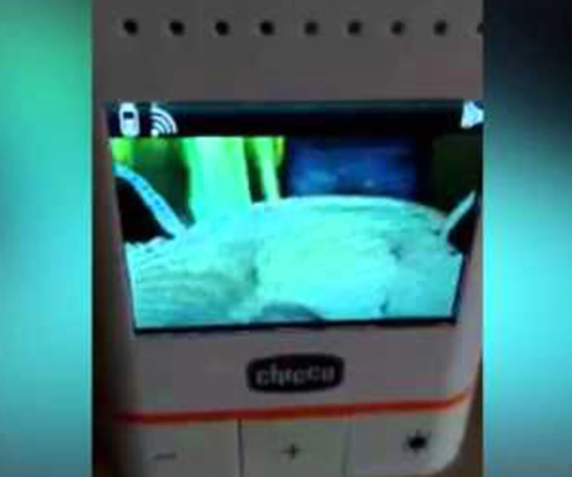 Baby monitor showing a crib, alleged apparition, with a blurry greenish image on screen in a dimly lit room.