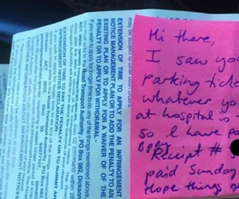 A parking ticket with a pink note attached, expressing empathy and stating the fine was paid by the note writer.