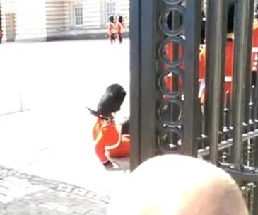 British guard slipping during changing of the guard at Buckingham Palace, with onlookers in the background.