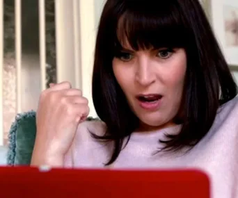 Woman with auburn hair looking surprised at a laptop screen, her fist raised in excitement or triumph.
