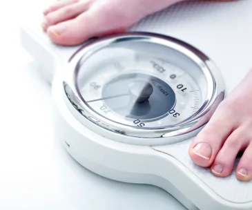 Close-up of feet on a bathroom scale showing measurement in kilograms.